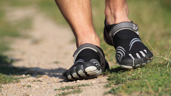 Photo a man's feet walking with foot glove shoes on a dirt path