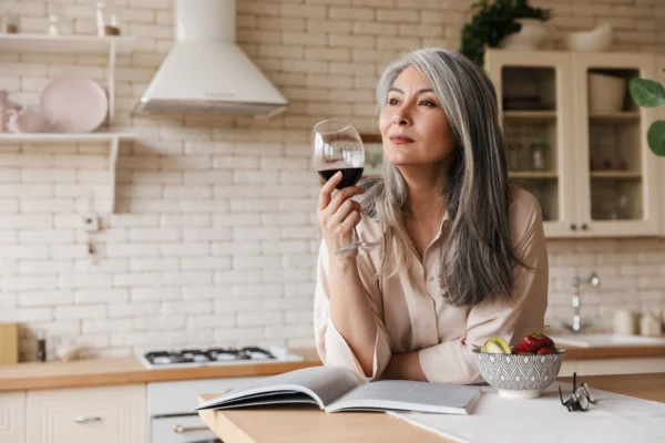 Woman leaning over kitchen counter drinking wine.