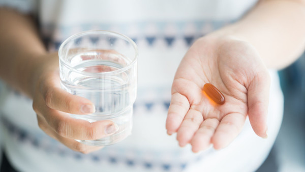 View of woman's hands holding a glass of water and a fish oil pill