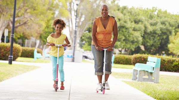 A grandmother and her granddaughter riding scooters in the park