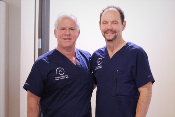 Photo of Regenexx founders Dr. Chris Centeno and Dr. John Schultz wearing blue medical scrubs and looking towards the camera.